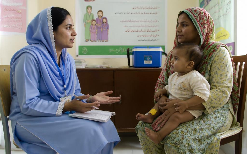 Lady health visitor counselling a mother holding her baby in a community health clinic